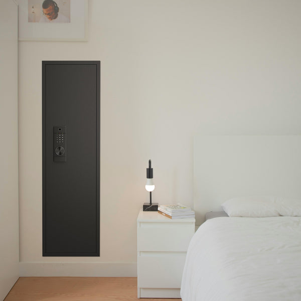 SLATE Biometric wall gun safe in black, installed flush in a bedroom wall beside the bed and nightstand