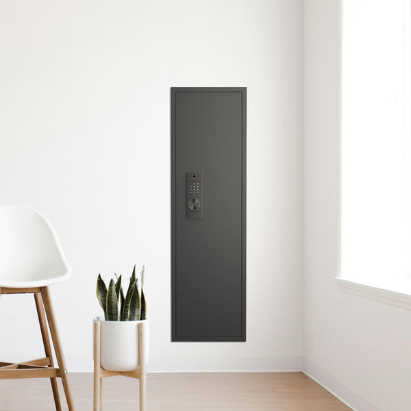 SLATE Biometric wall gun safe in black, installed flush in a living room corner wall beside a chair and plant