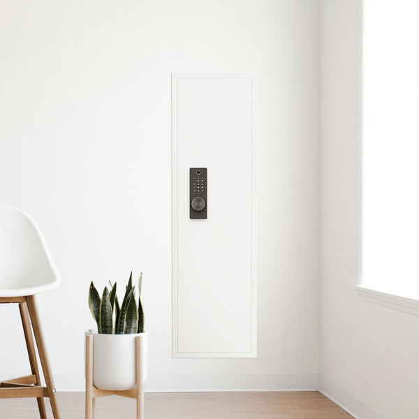 SLATE Biometric wall gun safe in white, installed flush in a corner wall beside a chair and plant